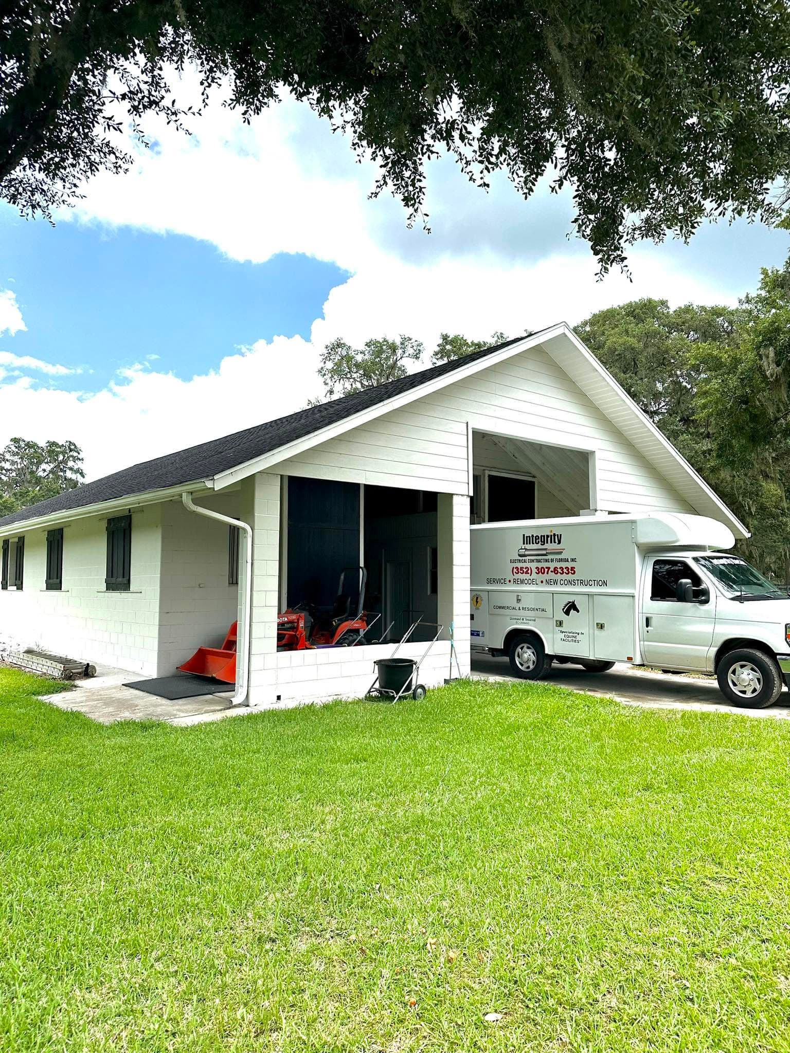 An Integrity Electrical Contracting work van parked in the driveway of a white house with a carport, under a large oak tree.