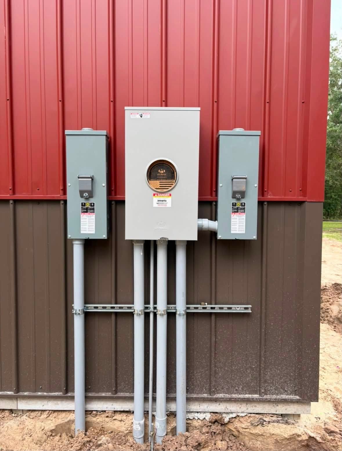 A meter base with two disconnect panels mounted on the red and brown metal wall of a barn, with conduit running down into the ground.