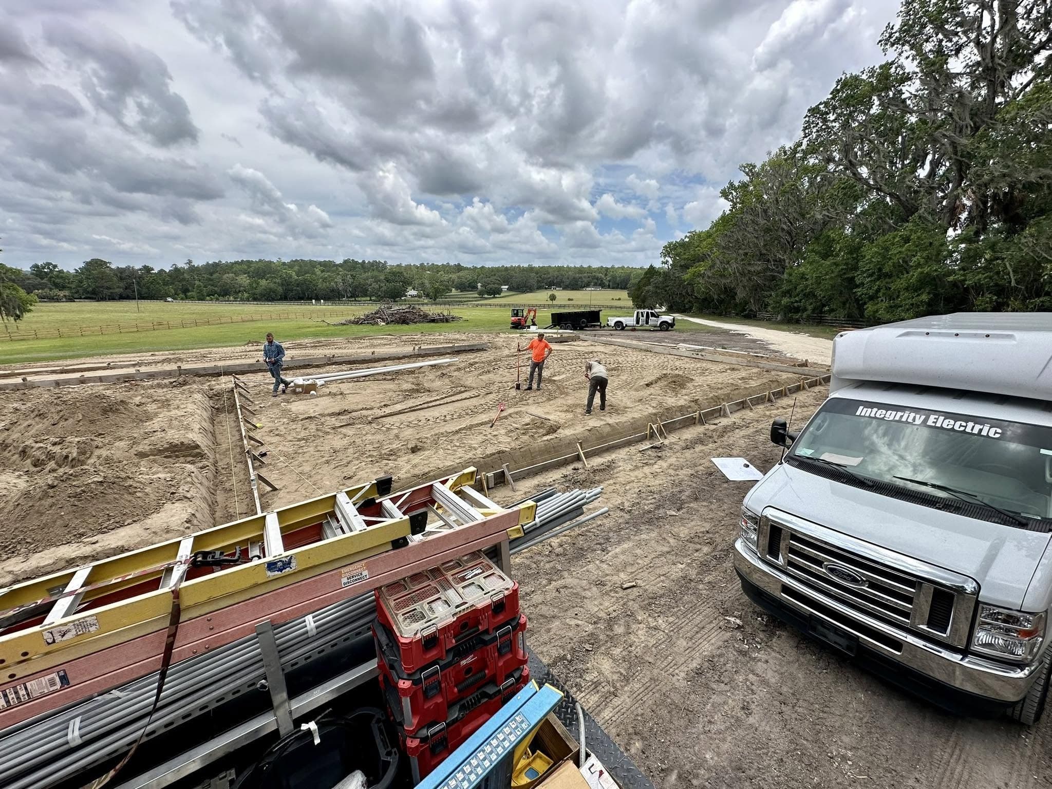 A white Integrity Electric van in the foreground of a large excavation site where crew members are laying out conduit runs.